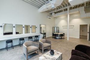 Modern salon interior with mirrors, black stools, and comfortable seating in neutral tones.
