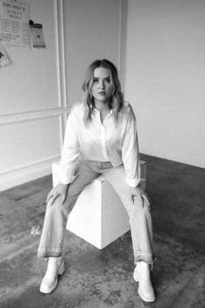 Black and white portrait of person in white shirt and jeans seated on geometric pedestal.