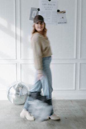 Motion blur portrait in casual attire against white paneled wall with disco ball.