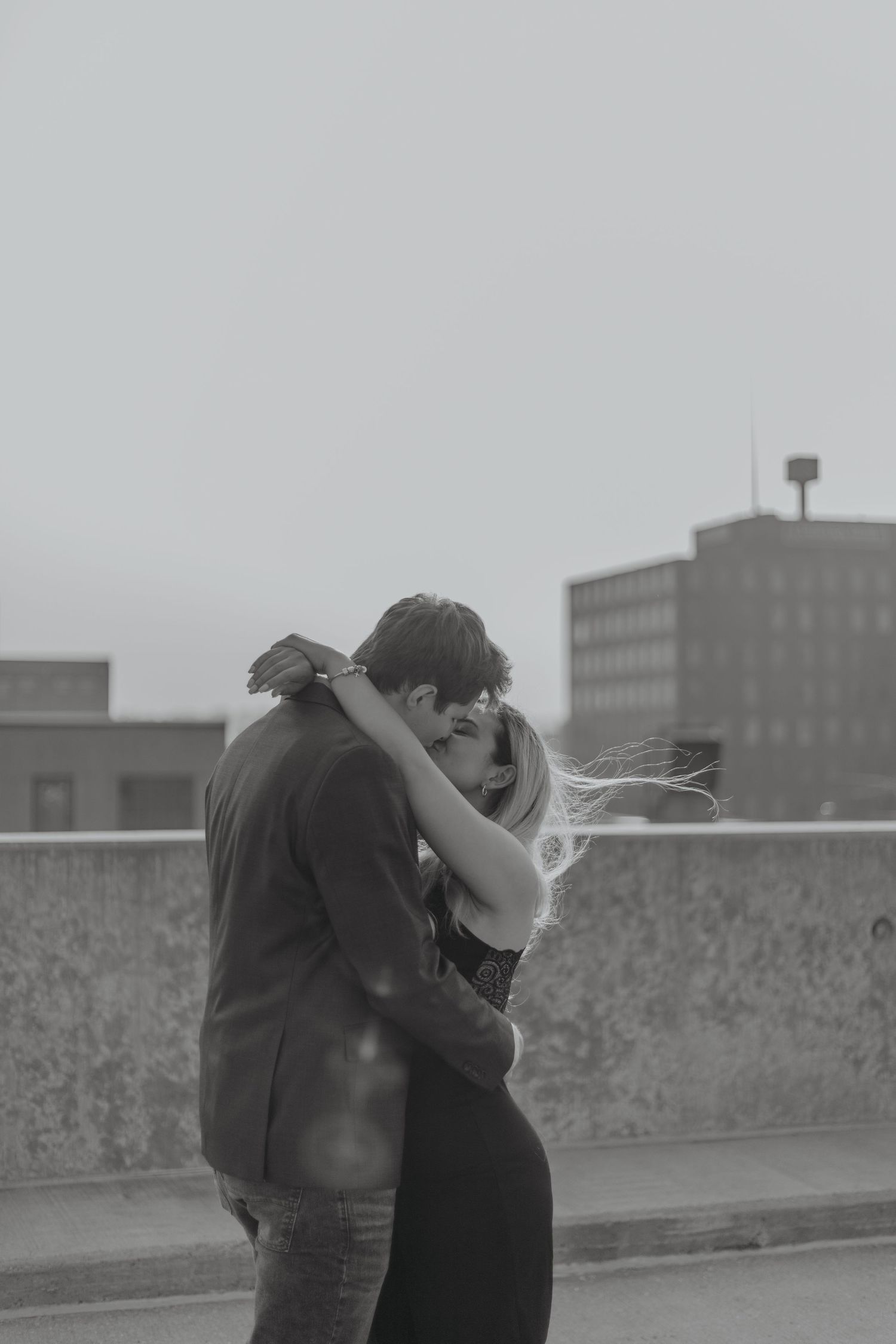 Couple embracing in black and white photo on city rooftop.
