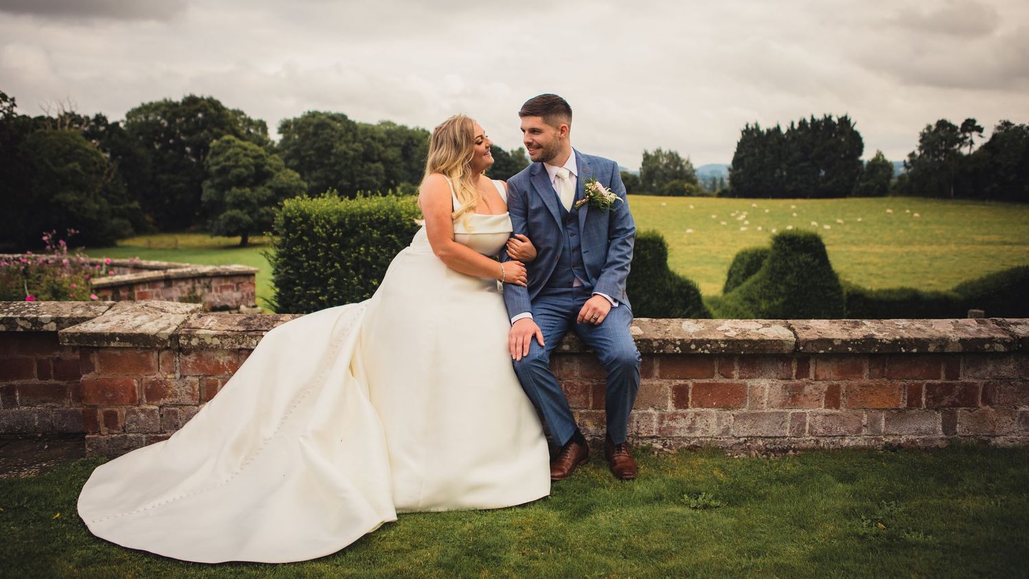 bride and groom sitting together on wall holding arm