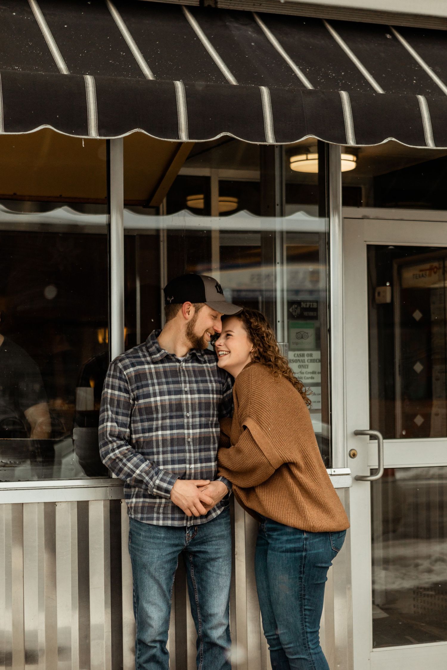 Couple sharing intimate moment outside storefront with striped awning.