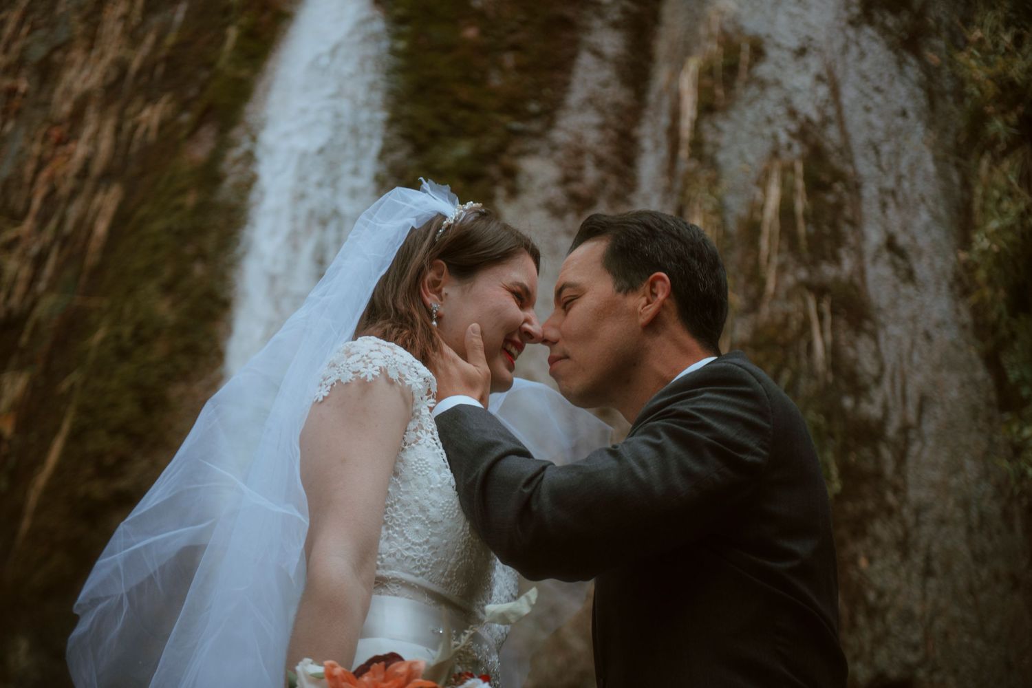 A romantic wedding moment captured in front of a majestic waterfall with the couple sharing a tender kiss.