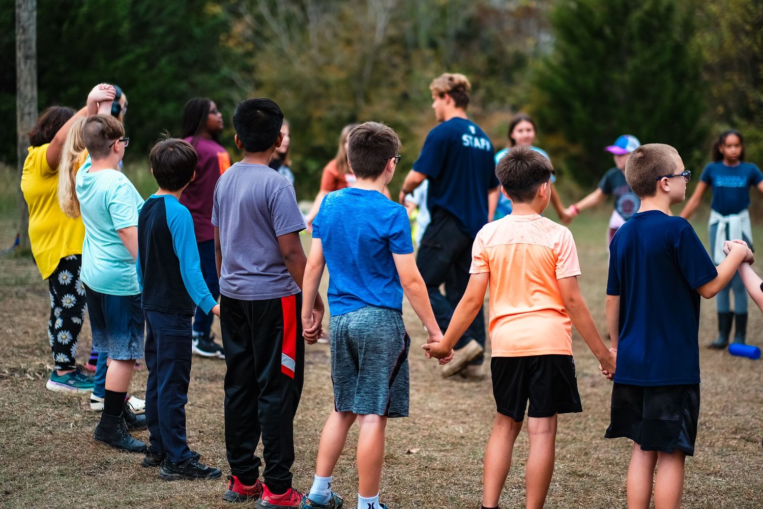 A group of school aged children hold hands to complete a team building challenge at Collin County Adventure Camp