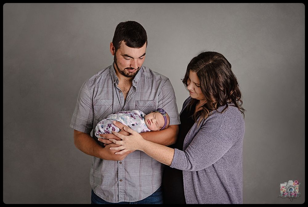 Parents cradling newborn baby during studio photoshoot.