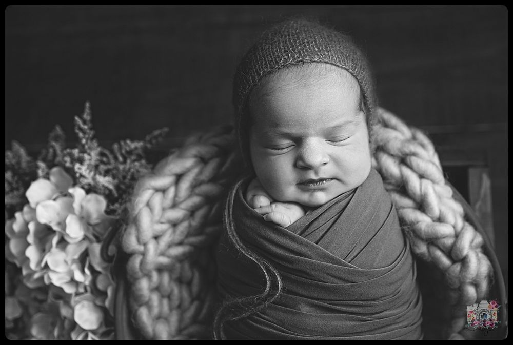 Black and white portrait of sleeping newborn with knit wrap and flowers.