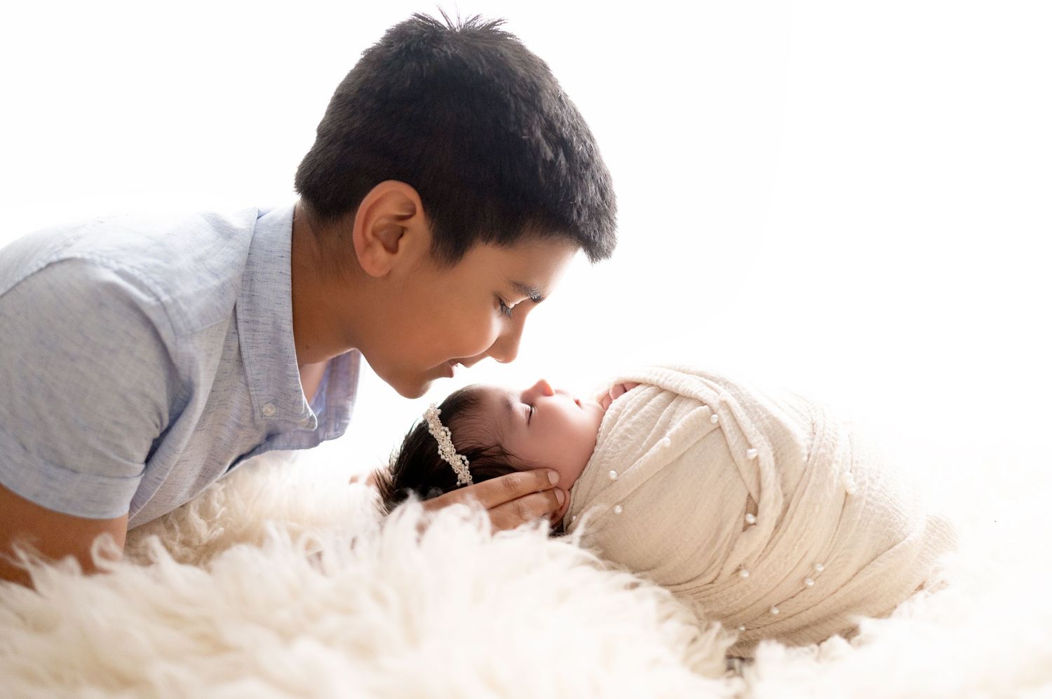 A tender moment between a person and sleeping newborn on soft white fur backdrop.