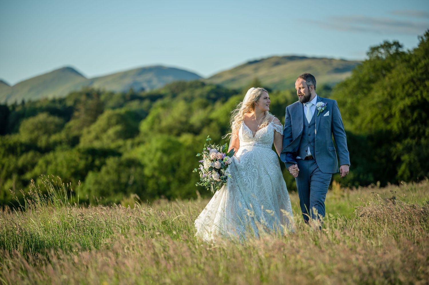 Bride and groom walking in meadow during Lake District wedding