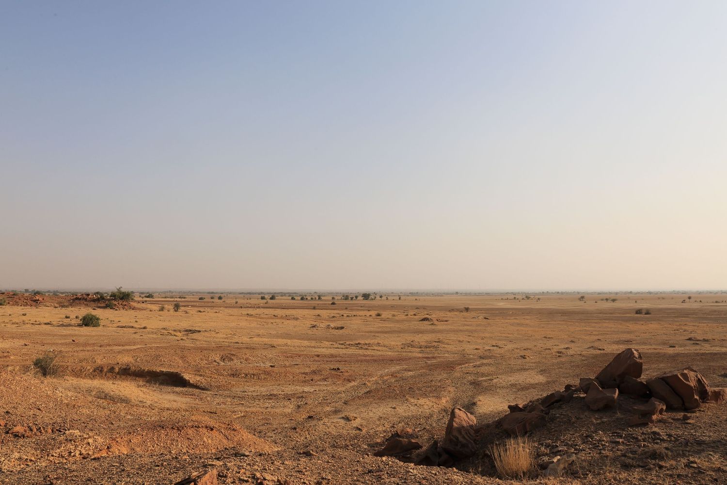 Arid desert landscape stretches to the horizon under clear skies with scattered rocks in the foreground.