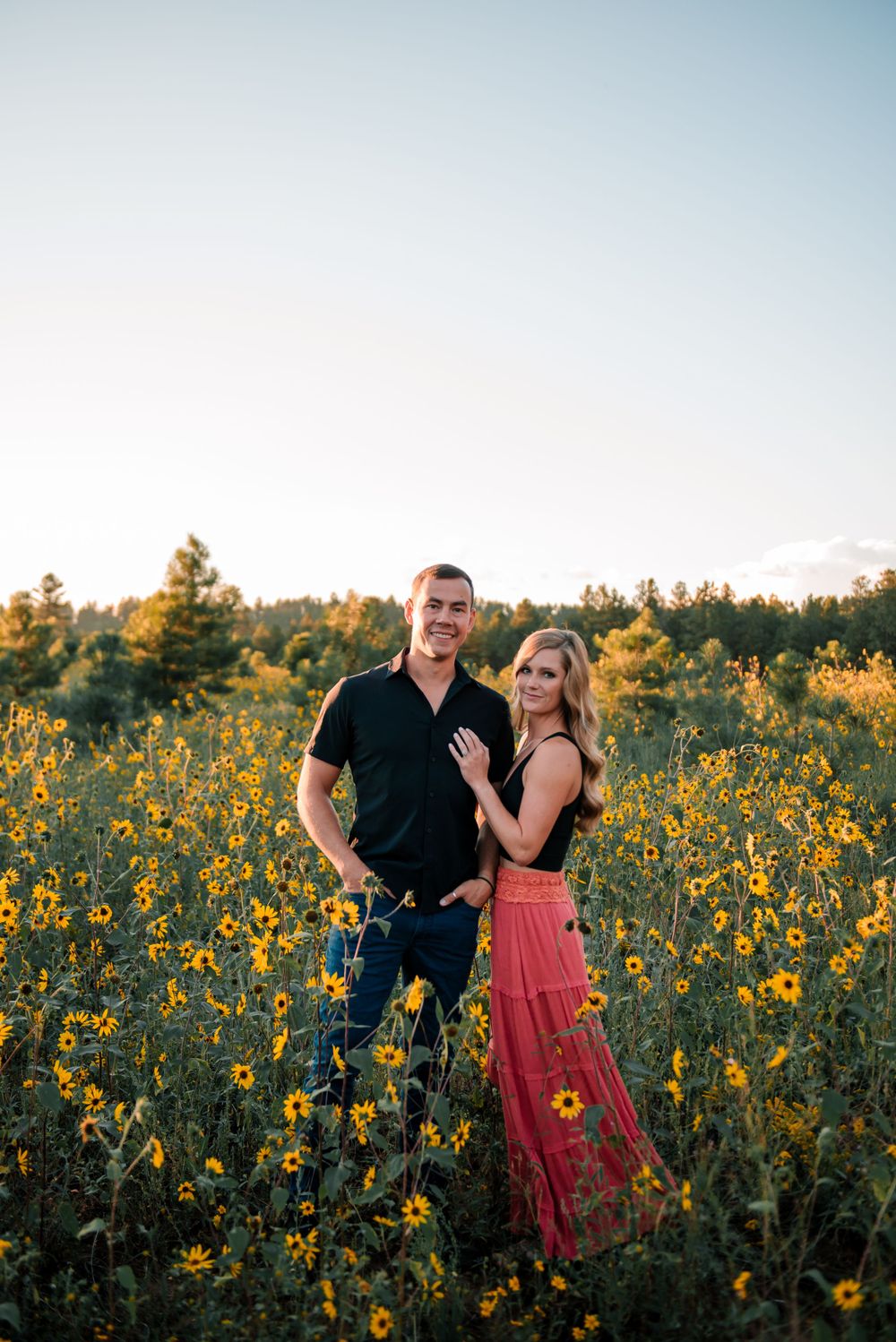Romantic couple embracing in a field of bright yellow sunflowers during golden hour.