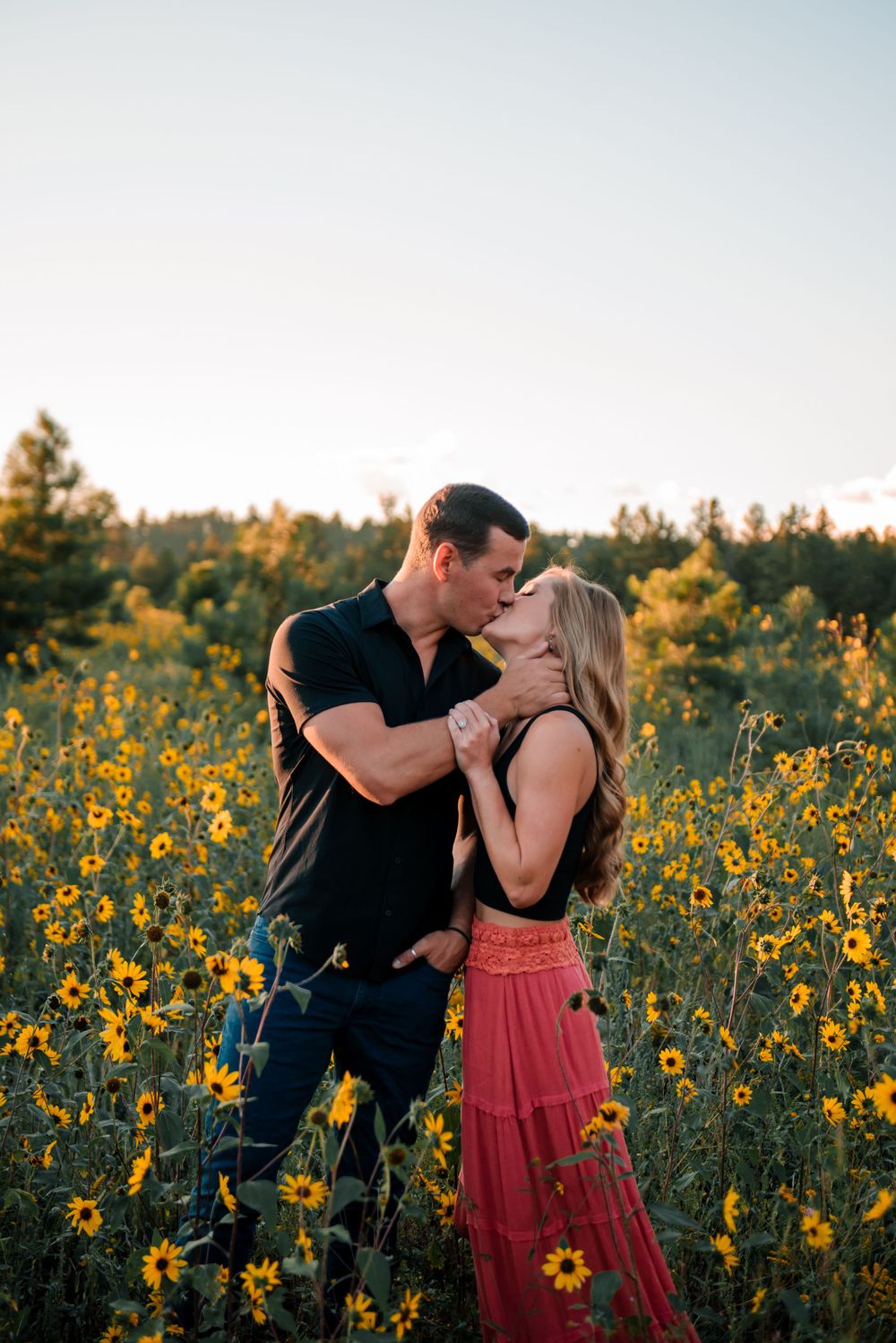 Intimate moment between a couple surrounded by tall sunflowers at sunset.