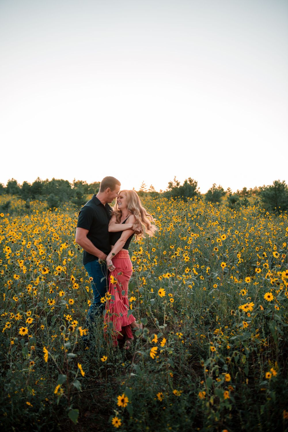 Couple embracing in a sunflower field during golden hour.