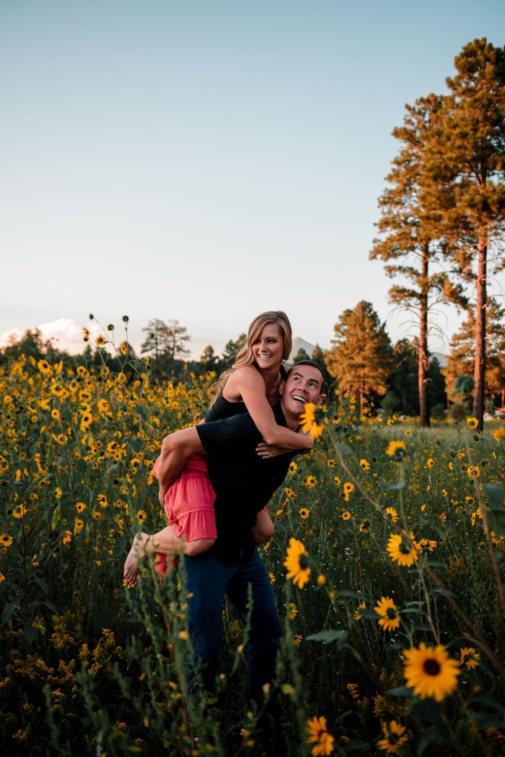 Playful couple laughing together in a field of bright yellow sunflowers.