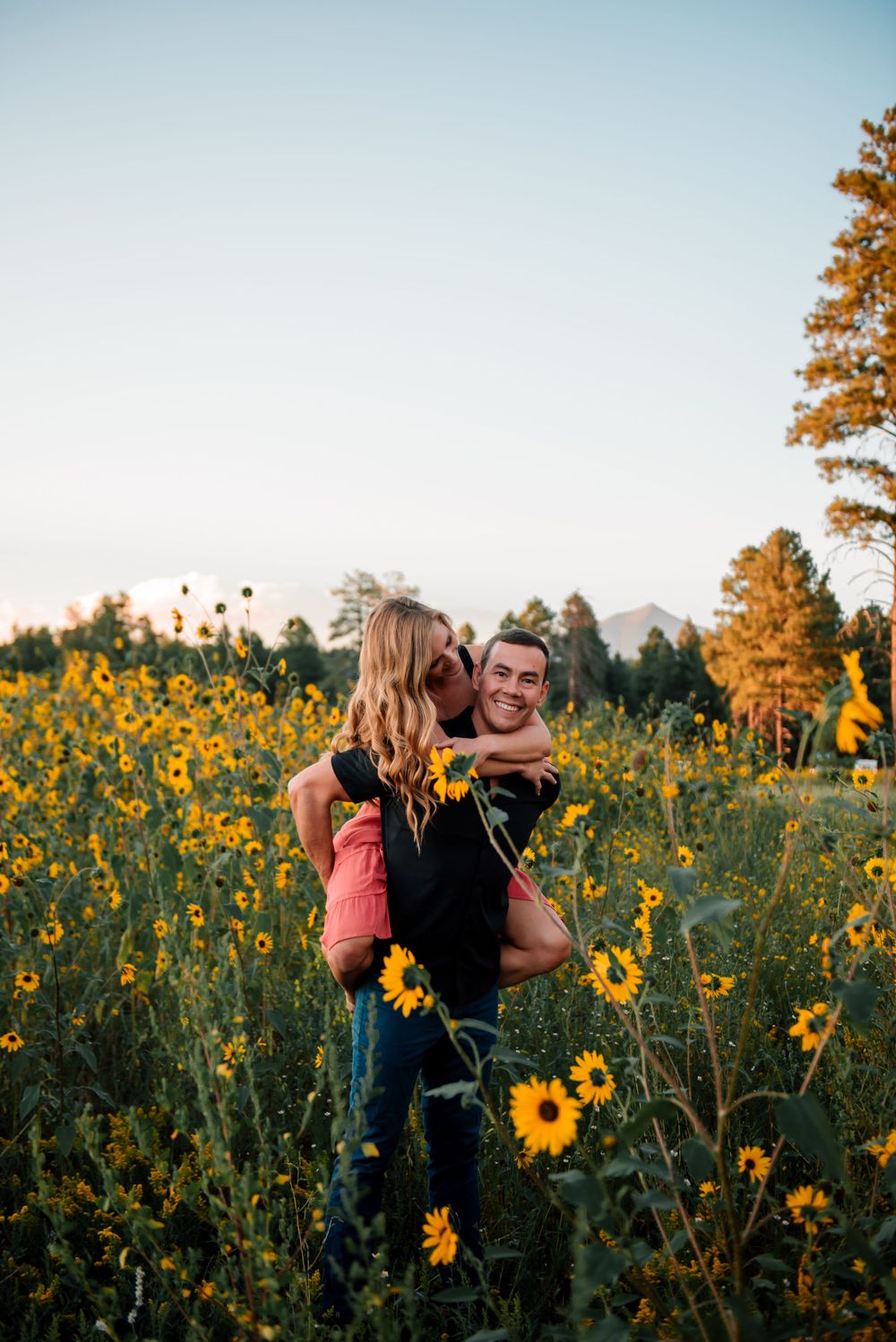 Couple embracing and laughing in a sunflower field during golden hour.