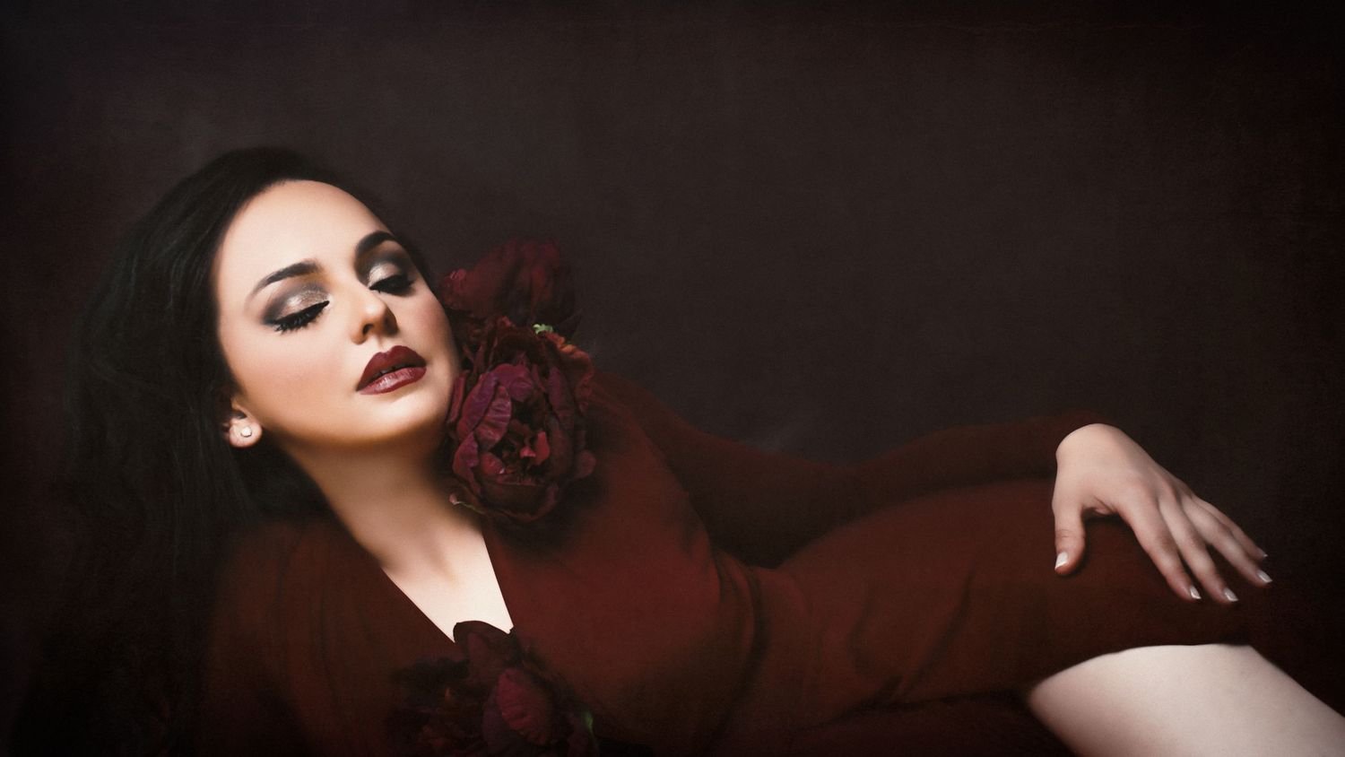 A glamorous portrait in deep burgundy tones with dramatic lighting against a dark background.