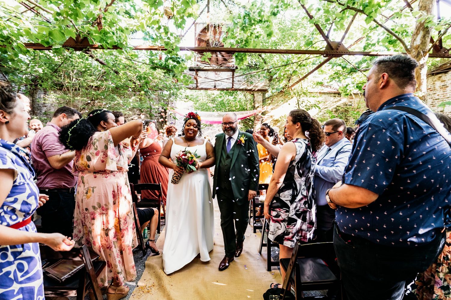Wedding ceremony in greenhouse venue with guests lining the aisle.