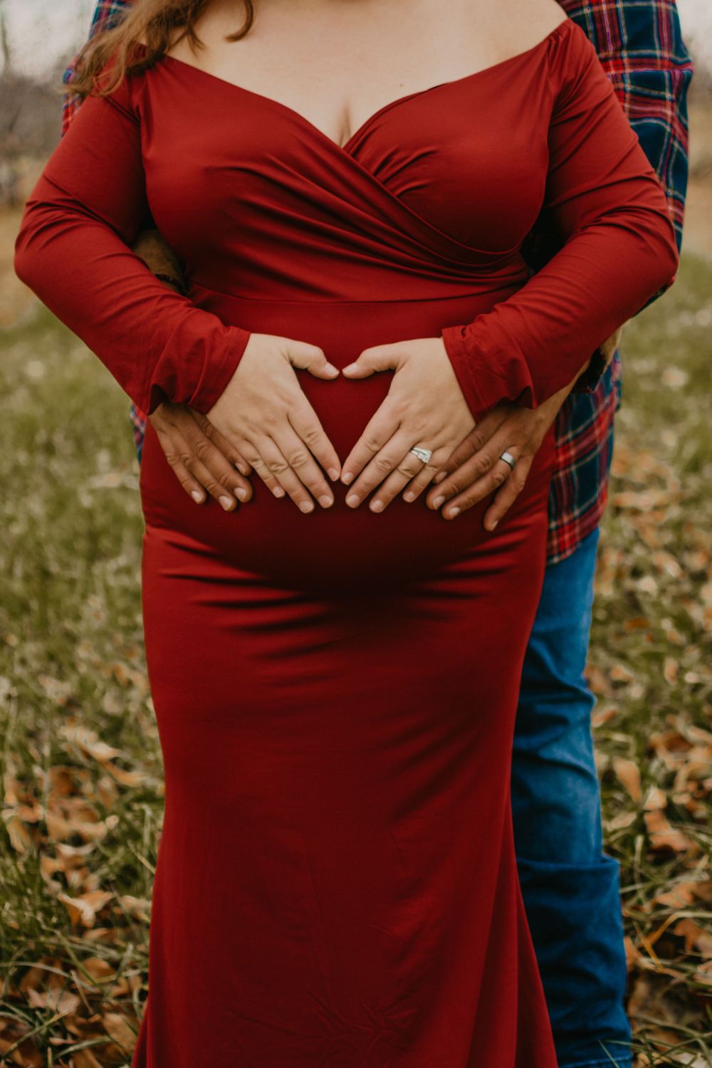 A maternity photo series showing a couple in a red dress and plaid shirt posing together in fallen autumn leaves.