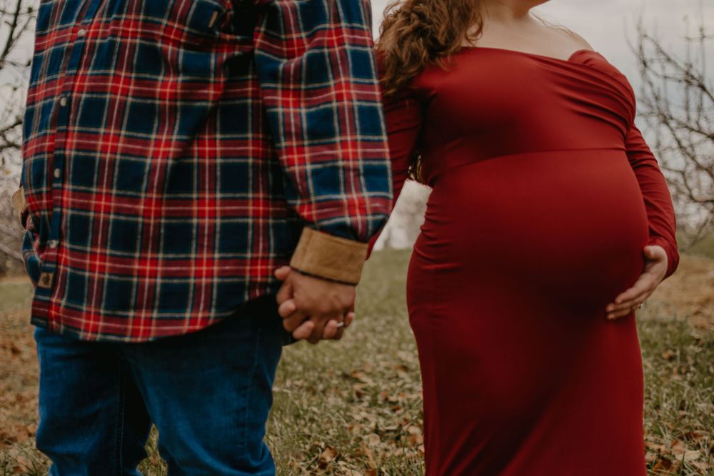 Close-up maternity photos showing hands forming a heart shape over a burgundy dress.