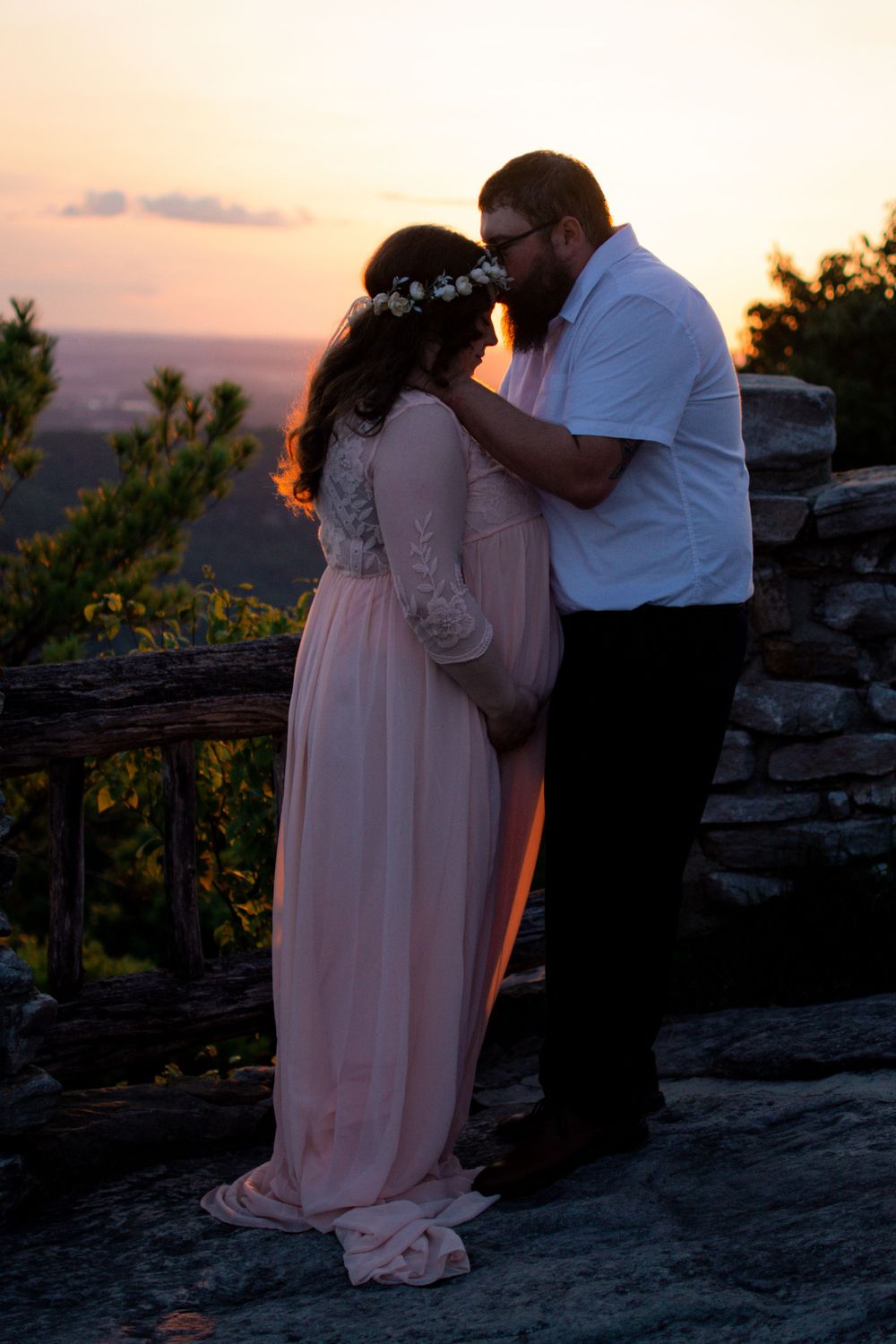 A couple shares an intimate moment during sunset on a rocky overlook.