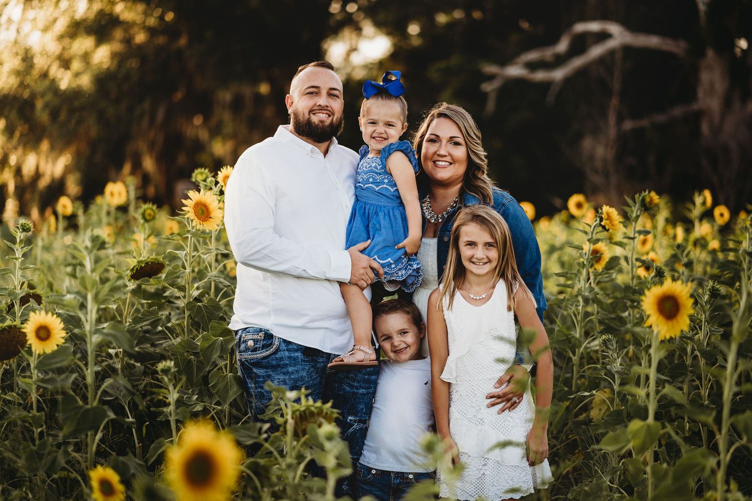 Family portrait in vibrant sunflower field during golden hour sunset.
