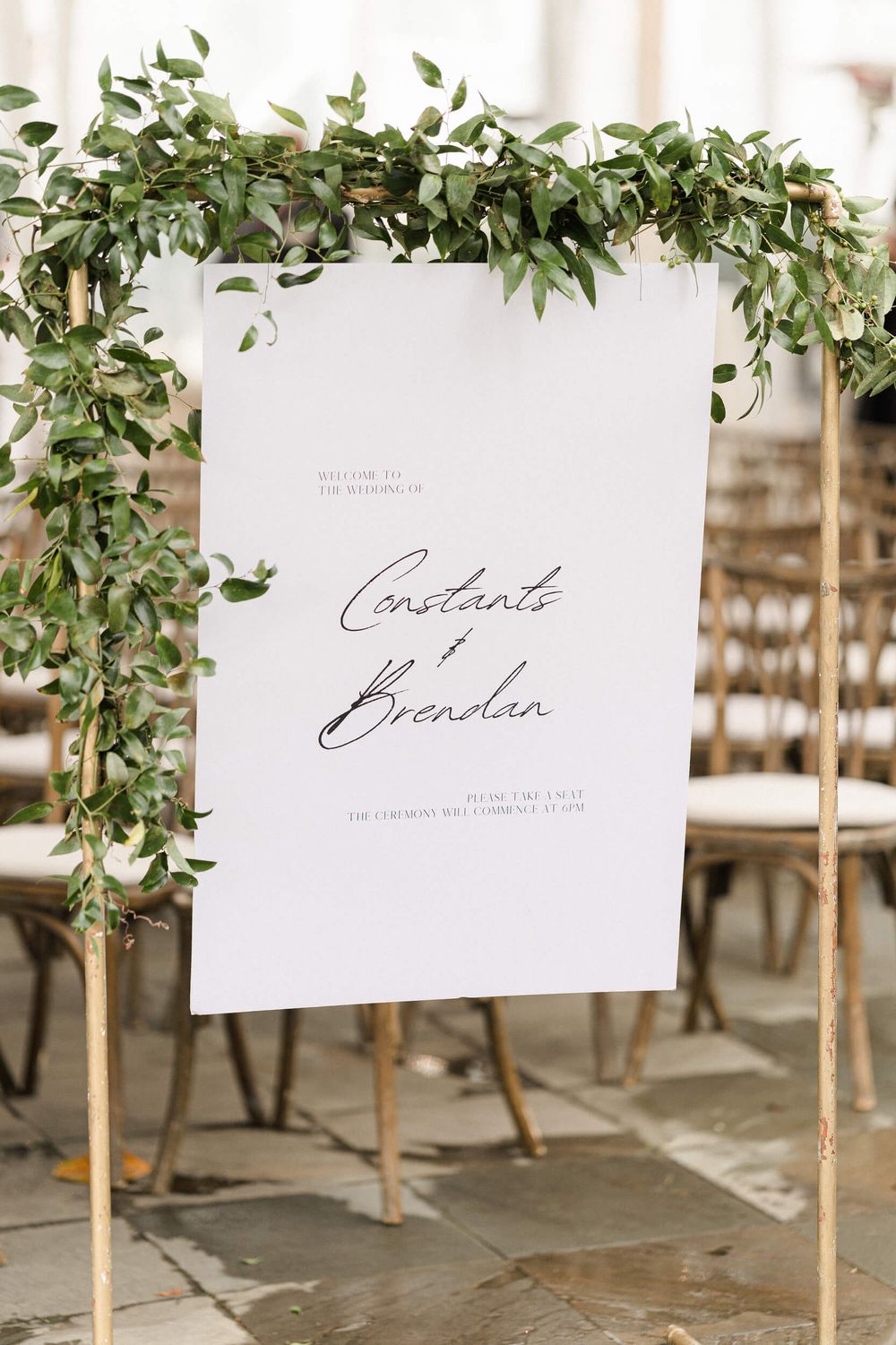 Wedding welcome sign with greenery garland and calligraphy displayed on gold stands.