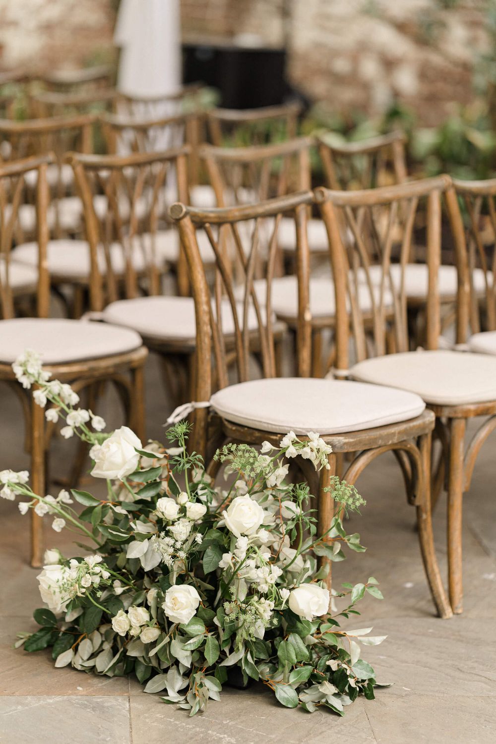 Cross-back wooden chairs with white cushions arranged with floral aisle decorations.