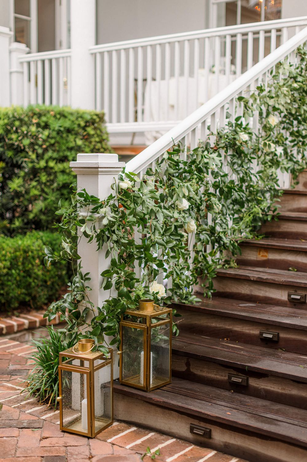 Elegant staircase decorated with cascading greenery and gold lanterns for a wedding.