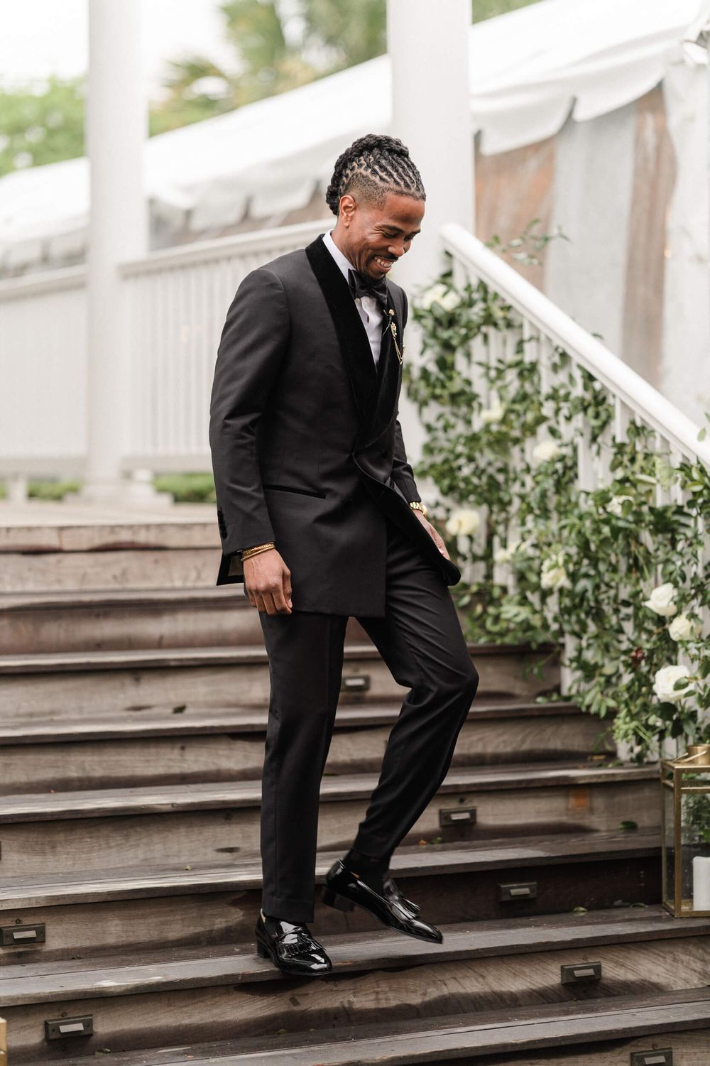 Person in formal black tuxedo walking down decorated outdoor stairs.