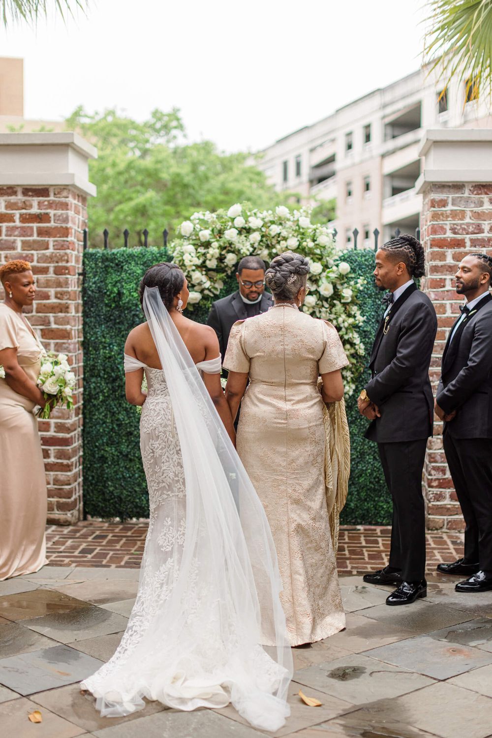 Outdoor wedding ceremony gathering with brick pillars and flowing white gown.