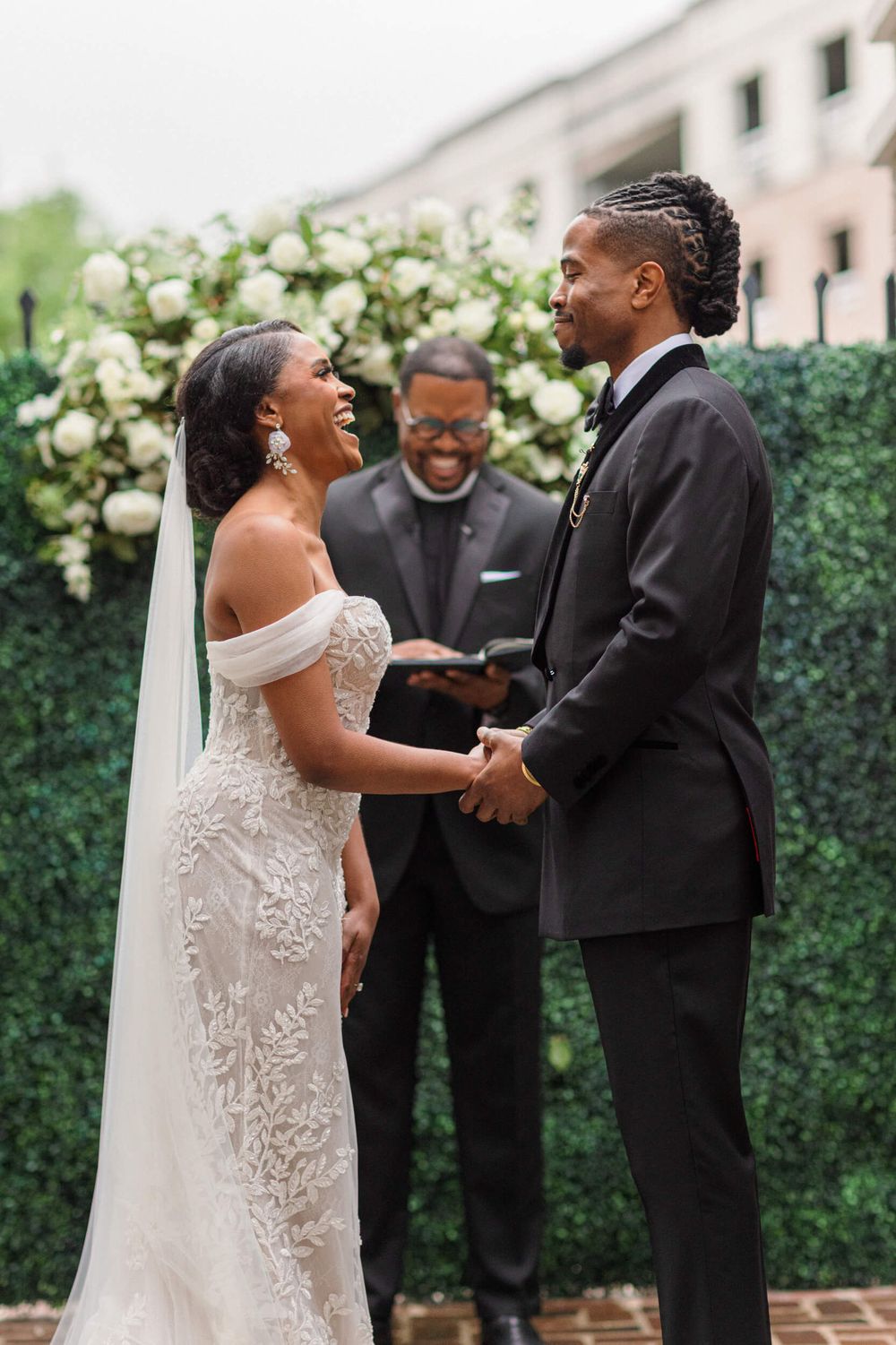A joyful wedding ceremony takes place in a garden setting with white floral decorations.