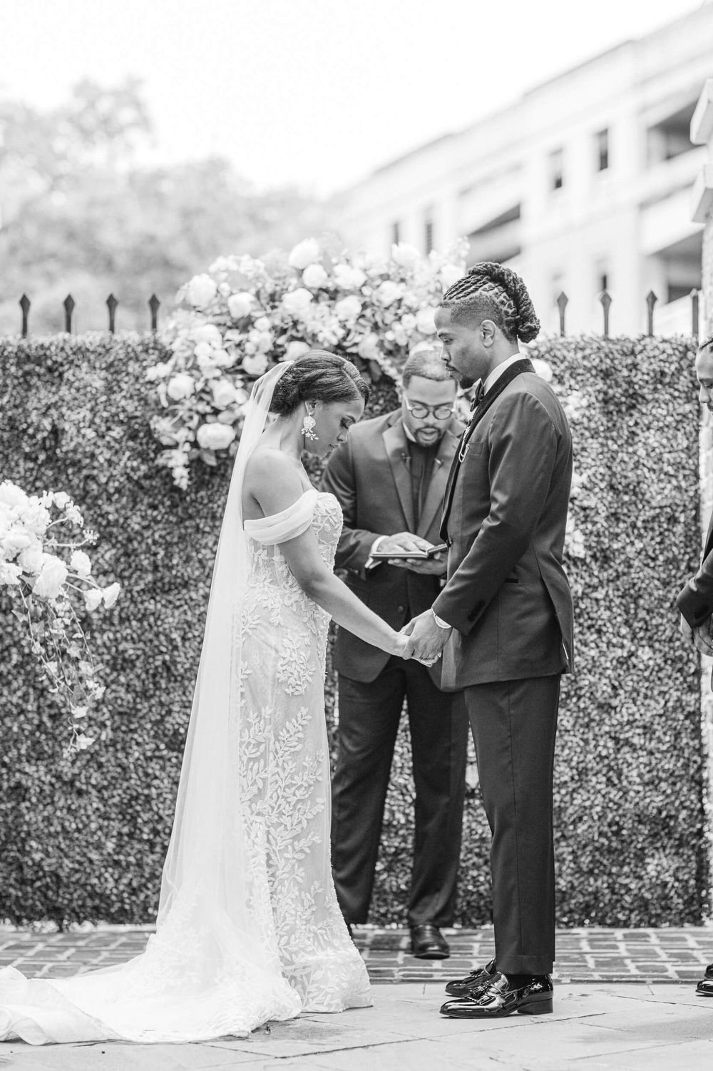 Black and white photo of a wedding ceremony in front of an elegant hedge wall with floral arrangements.