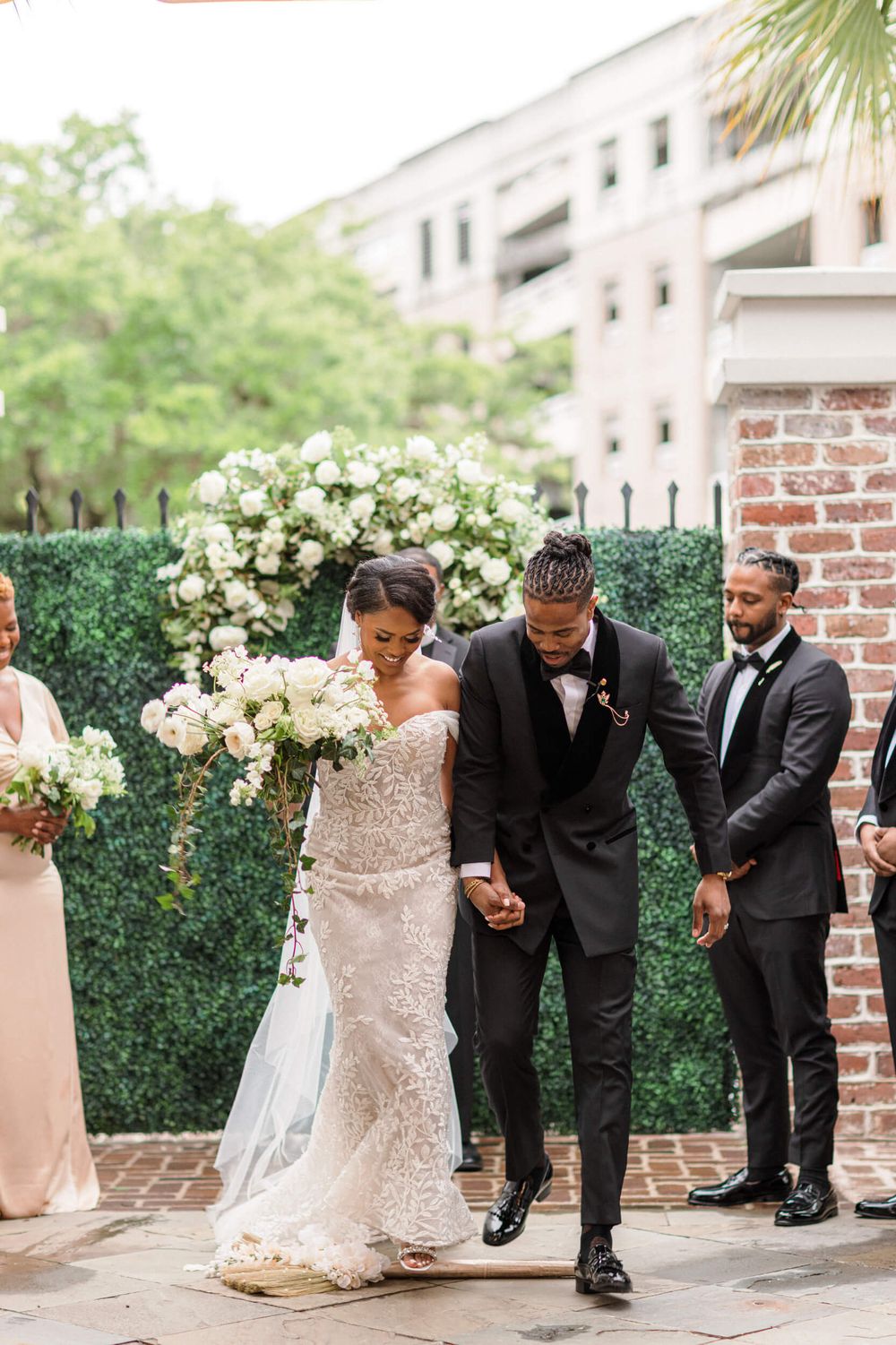 Wedding ceremony exit with floral hedge backdrop and brick columns in an outdoor setting.