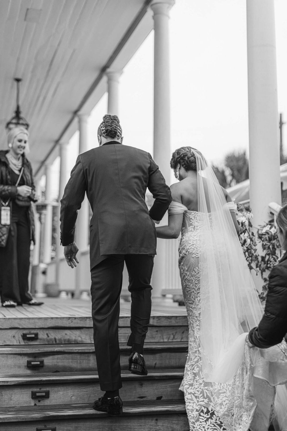 Black and white photo of couple ascending stairs with elegant white columns in background.