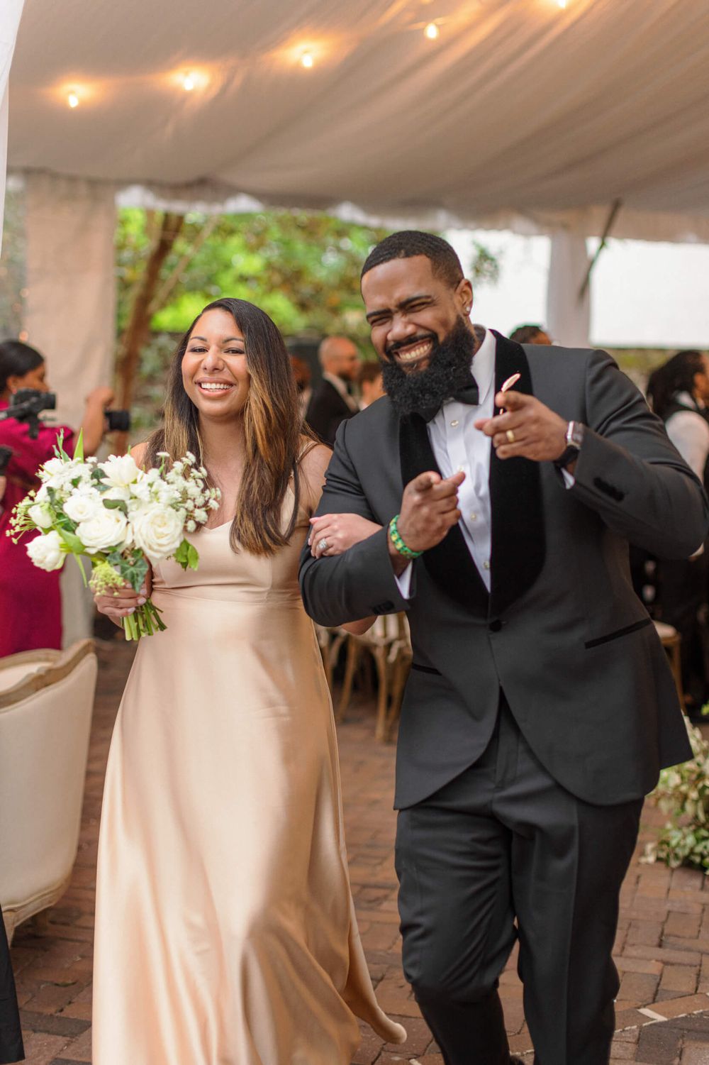 Celebratory moment at wedding with attendants in champagne gown and dark suit walking arm in arm.