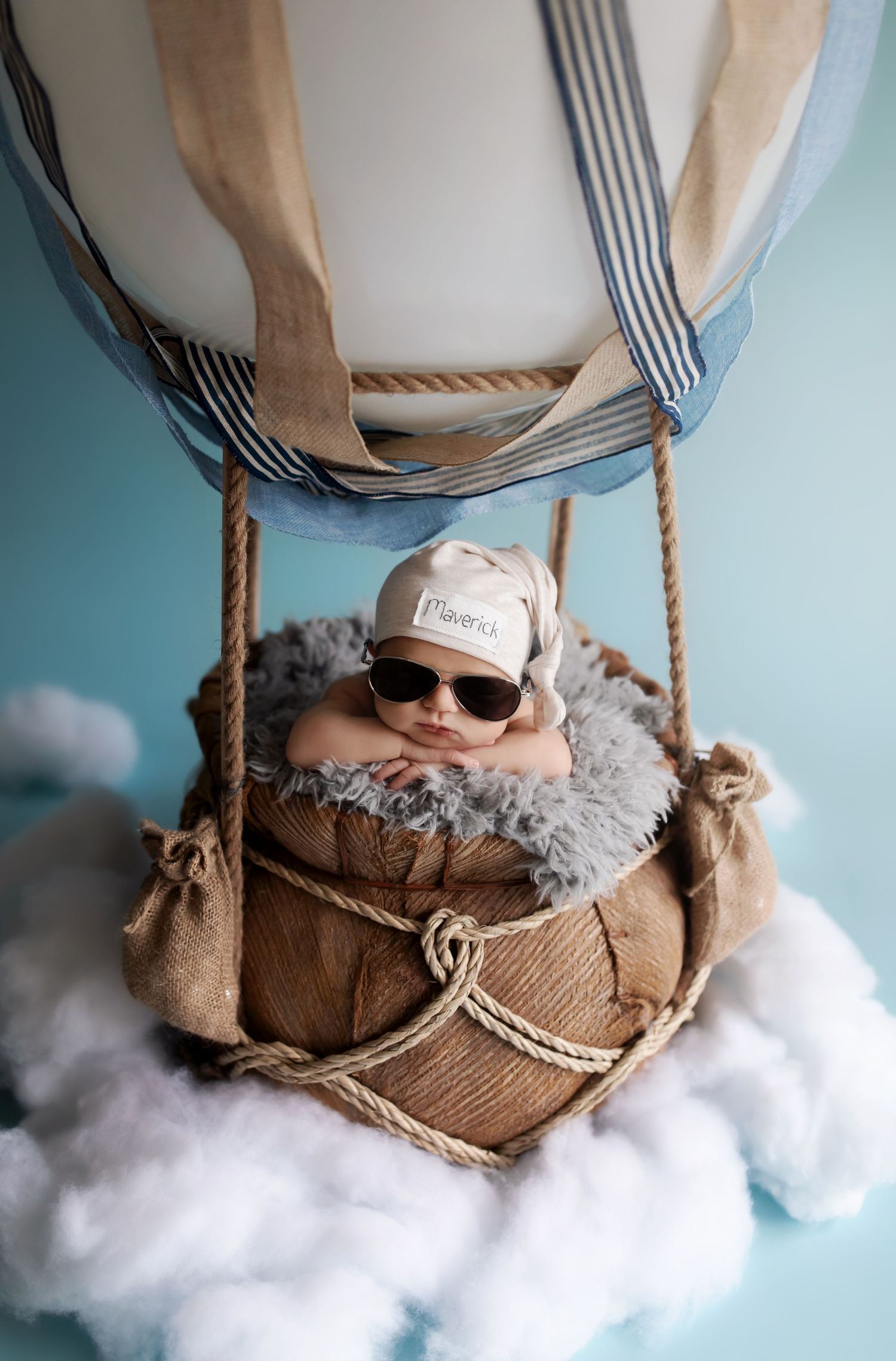 Creative hot air balloon nursery setup with plush clouds and ropes against blue wall.