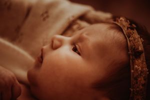 Moody sepia close-up portrait of a baby with crown against dark background.
