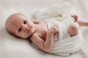 Series of artistic newborn baby photographs in soft white wrapping.