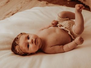 Artistic sepia-toned portrait of a baby wearing a delicate crown lying on soft bedding.