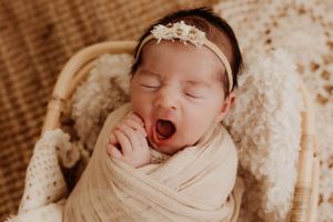 Peaceful newborn baby sleeping in soft beige wrap with delicate lace details.