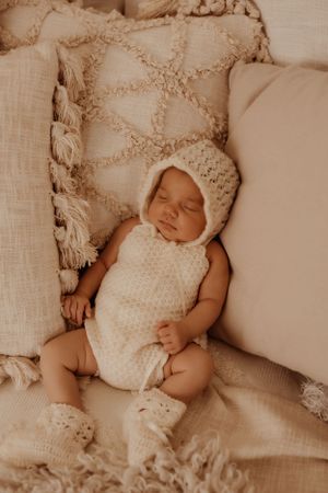 Peaceful newborn sleeping on white cushions wearing knit outfit.