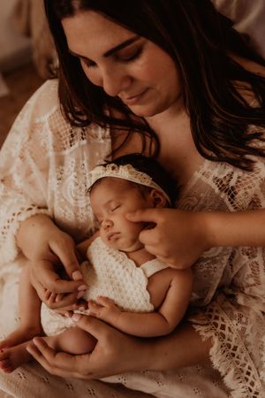 Tender moment between mother in lace dress holding sleeping newborn.