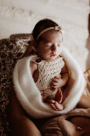 Newborn baby resting in white fuzzy blanket with crocheted wrap and headband.