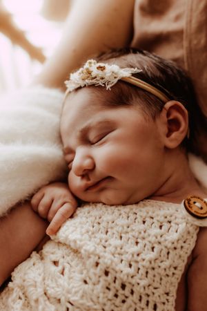 Sleeping infant nestled in cream knitted wrap with delicate textures.