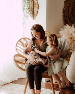 Parent and baby sharing intimate moments on rattan chair with pampas grass decor in background.