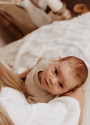 Baby wearing beige sweater lying on white bedding in various relaxed poses.