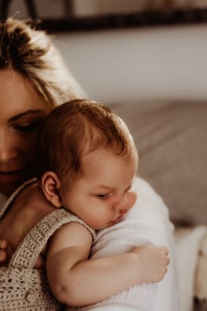 Tender moment of a baby in white lace clothing being cradled in warm sepia tones.