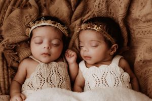 Two sleeping infants wearing matching lace outfits lying side by side in sepia tones.