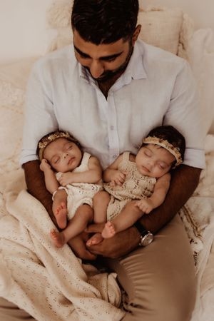 Peaceful moment of sleeping infants being held in white and neutral tones.