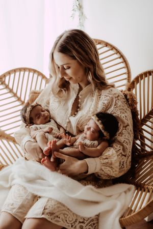 Nurturing moment captured in rattan chair with white lace clothing and natural lighting.