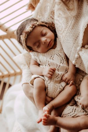 Baby in delicate lace dress sleeping peacefully on white textured bedding.